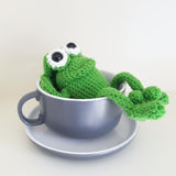 Happy looking green amigurumi crochet frog sitting on a white background