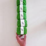 Stack of green yarn balled with The Pigeon's Nest sticker balancing on a hand