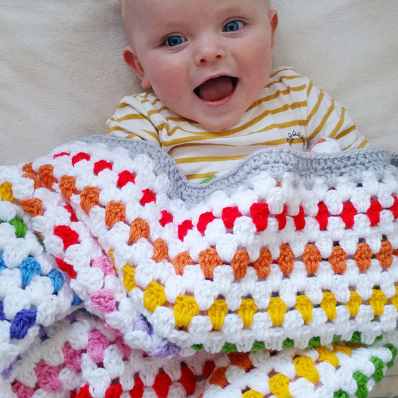 smiling baby under a white and rainbow striped crochet blanket