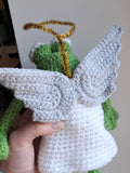 Handmade crochet angel toy with white wings and green body held by a person.