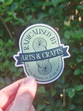 Sticker with 'Radicalised by Arts & Crafts' text held against a green leafy background