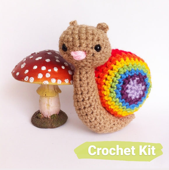 Small rainbow crocheted snail on a white background with a toadstool