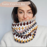 White woman with cowl pulled up over the bottom half of her face. the text in the top left orner lets you know this is the latte colourway