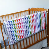 Rainbow crochet blanket haning on cot in nursery