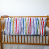 Finished handmade crochet rainbow stripe blanket hung lengthways down a cot side