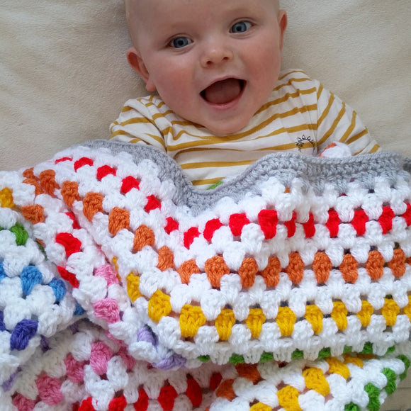Happy baby underneath a bright rainbow striped croceht blanket