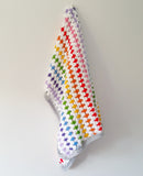 Rainbow crochet blanket hanging on a hook on a white wall