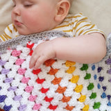 Sleeping chubby baby underneath rainbow crochet blanket