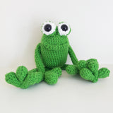 Happy loking green amigurumi crochet frog sitting on a white background