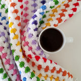 Crchet rainbow blanket on white table next to a cup of black tea